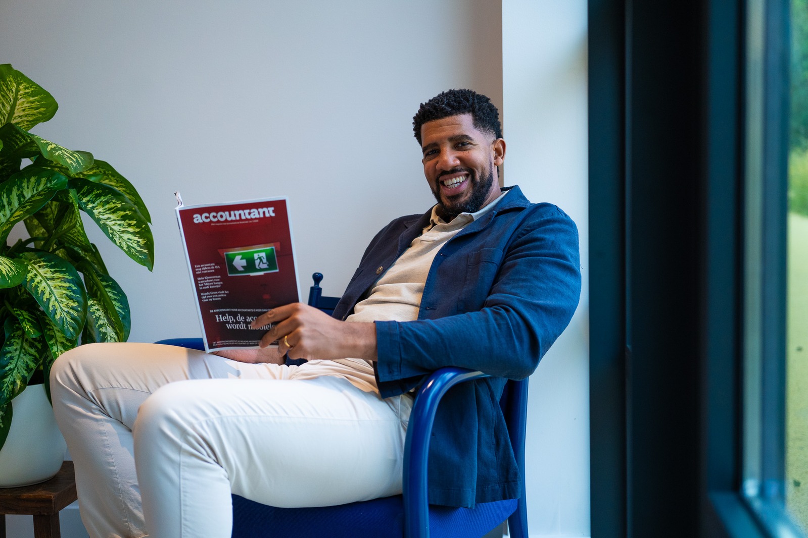 Man zit lachend in een blauwe stoel met een tijdschrift over accountancy